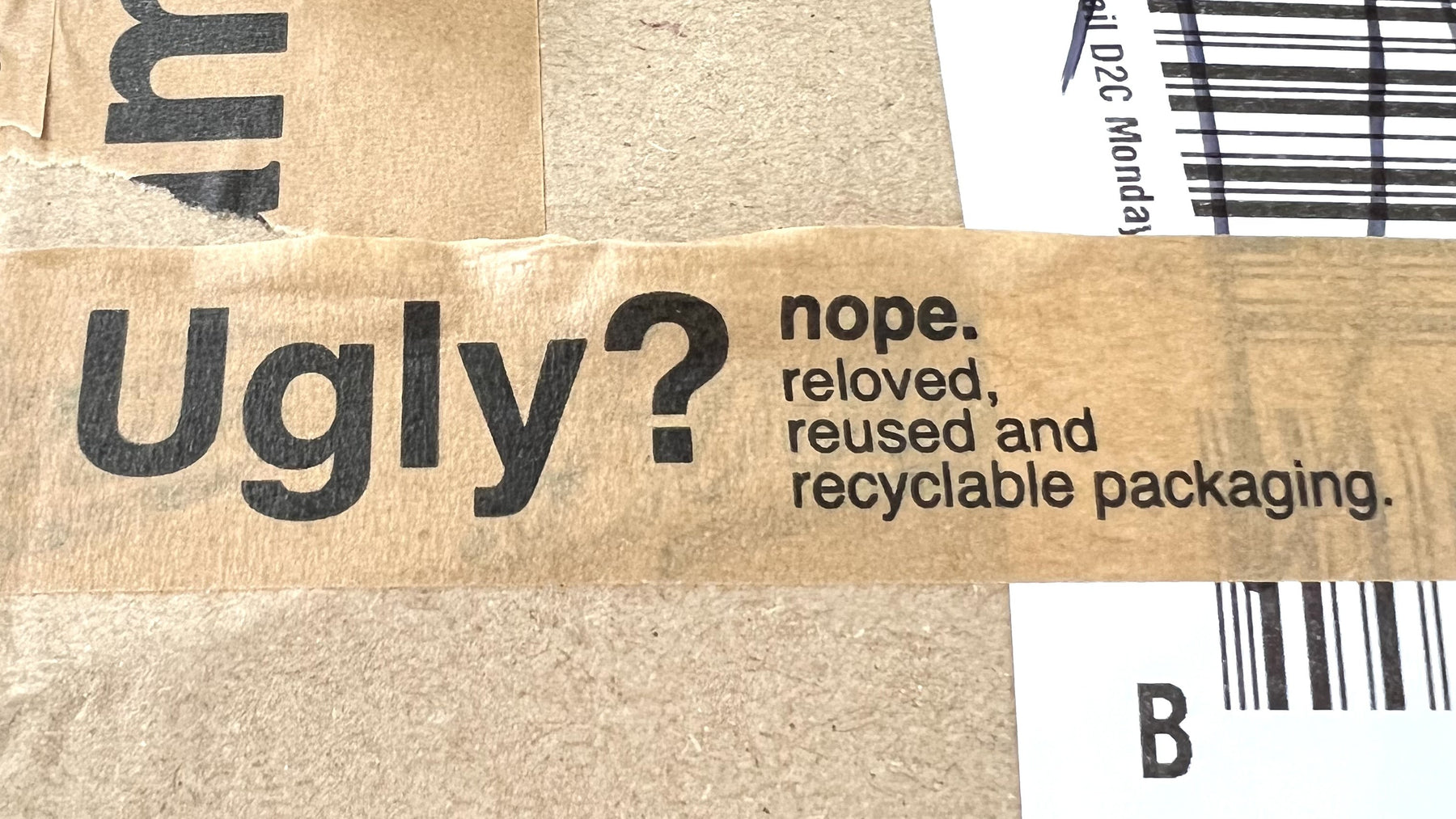 A close-up of brown kraft cardboard packaging tape printed with the text 'Ugly? nope. reloved, reused and recyclable packaging'.