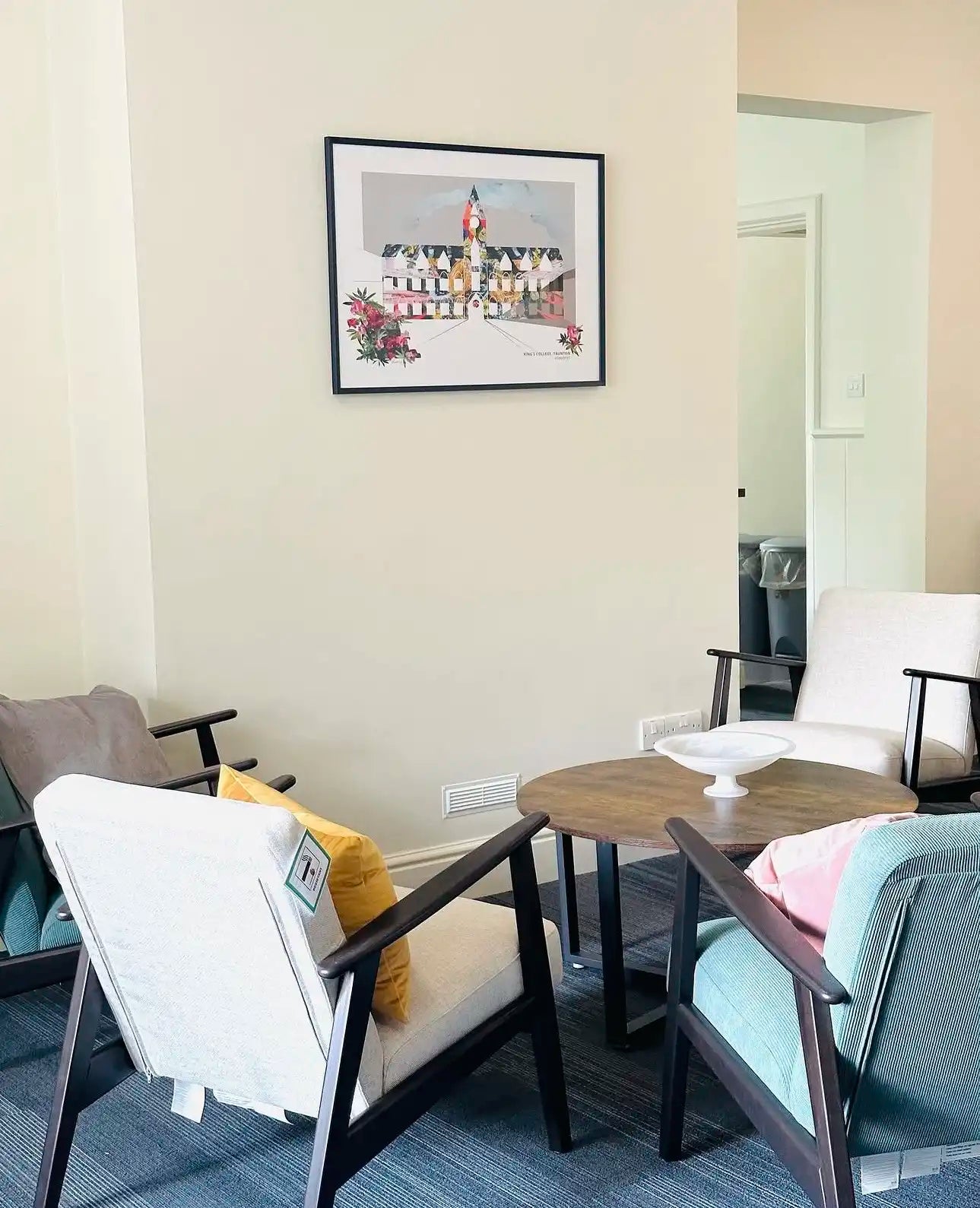 Corporate Landscape Art inside King's College, Taunton - A framed art print depicting a classic French chateau is displayed on a beige wall in a modern living room setting with three armchairs and a round wooden coffee table.