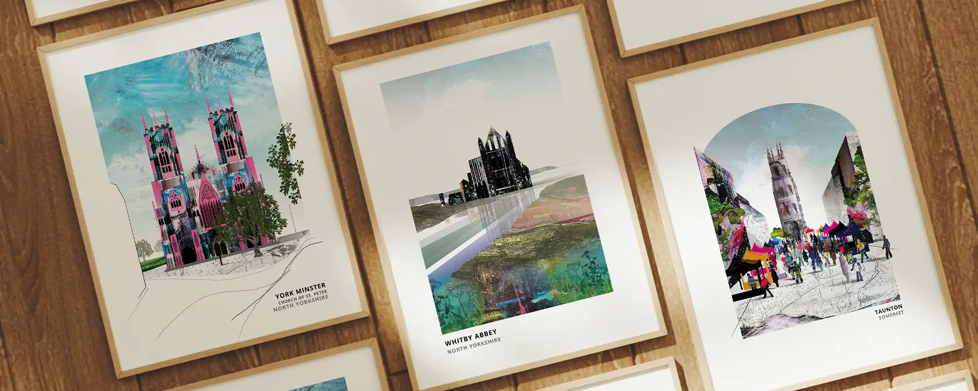 Three framed art prints with white mounts are displayed on a wooden wall. The prints feature colourful architectural sketches and watercolour-style city scenes in pink, blue, green, and grey tones.