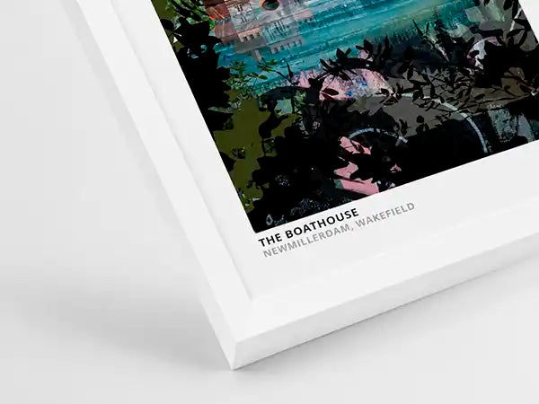 A framed art print shown at an angle on a light gray background. The print features a stylized illustration of 'The Boathouse' in New Milfordham, Wakefield, with dark foliage silhouettes and a teal-toned water scene.