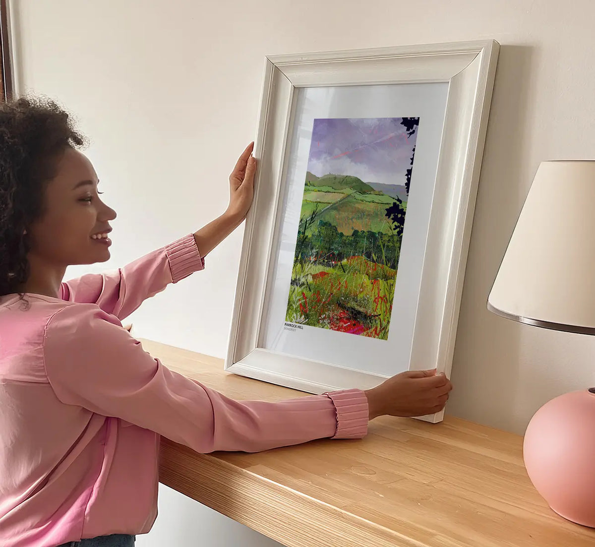 Parrock Hill art print by Vicki Shortt, the rounded green hill above patchwork fields near the Somerset and Dorset border, framed and propped on a sideboard in a room setting
